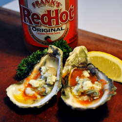 A bottle of Franks Red Hot sauce, with halved oysters with doused in butter hot sauce and crumbled blue cheese.