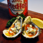 A bottle of Franks Red Hot sauce, with halved oysters with doused in butter hot sauce and crumbled blue cheese.