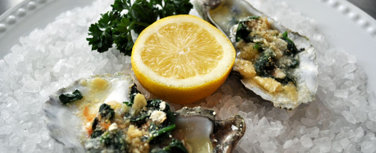 Picture of Oysters Rockefeller, lemon and parsley on a bed of rock salt.