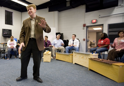 A person standing in a room with people seated in the background
AI-generated content may be incorrect.